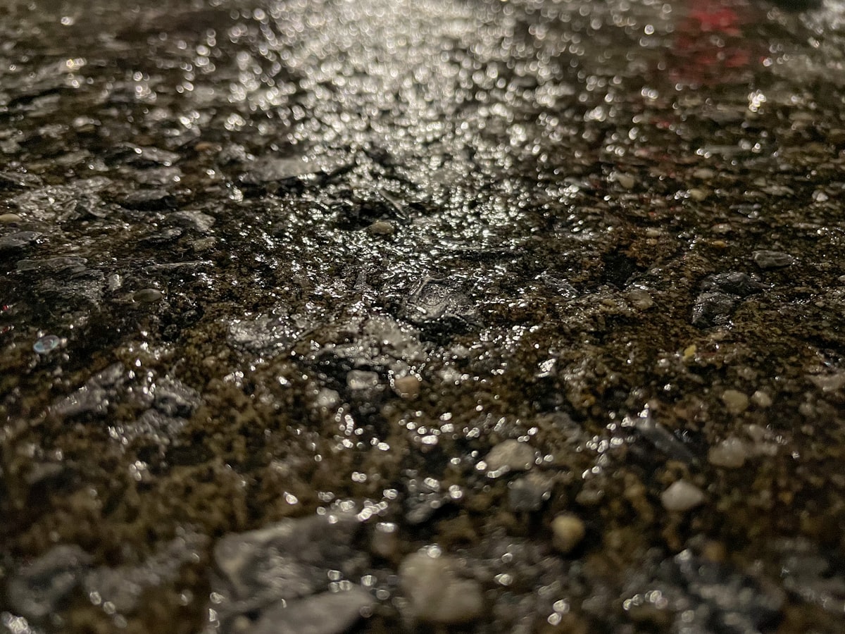 Close-up of white road salt crystals and de-icing grit staining a wet road surface — the source of driveway staining across DuPage County Illinois every winter